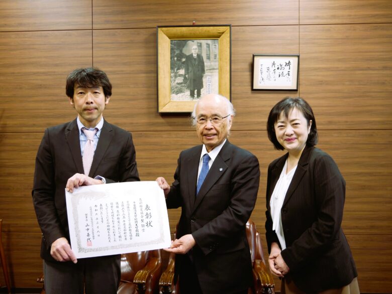 色彩検定協会 吉野勝さん（写真左）から、本学佐久間勝彦学長と沢谷有梨准教授（「色彩学」の授業を担当）に賞状が手渡されました